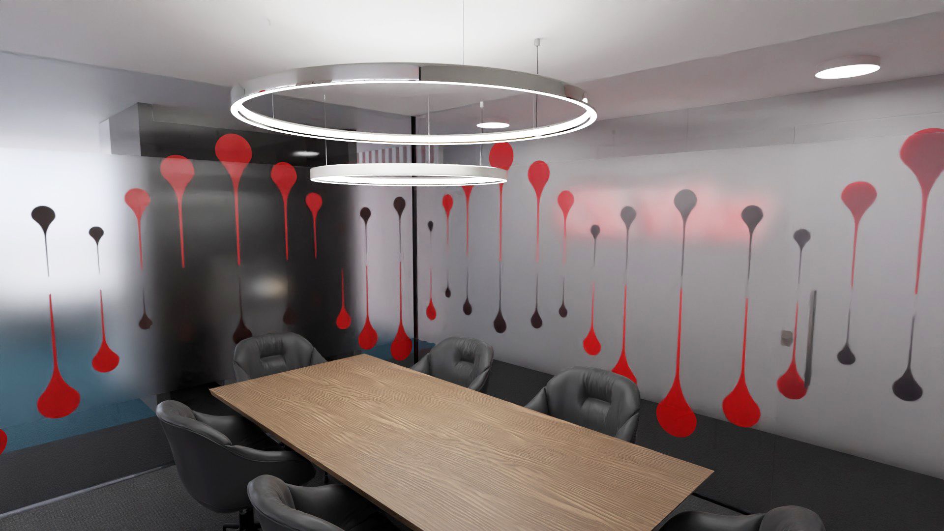Sala de reunião com mesa de madeira, cadeiras cinza escuras, candeeiros circulares duplos suspensos e paredes envolventes com os grafismos de gotas vermelhas e pretas.